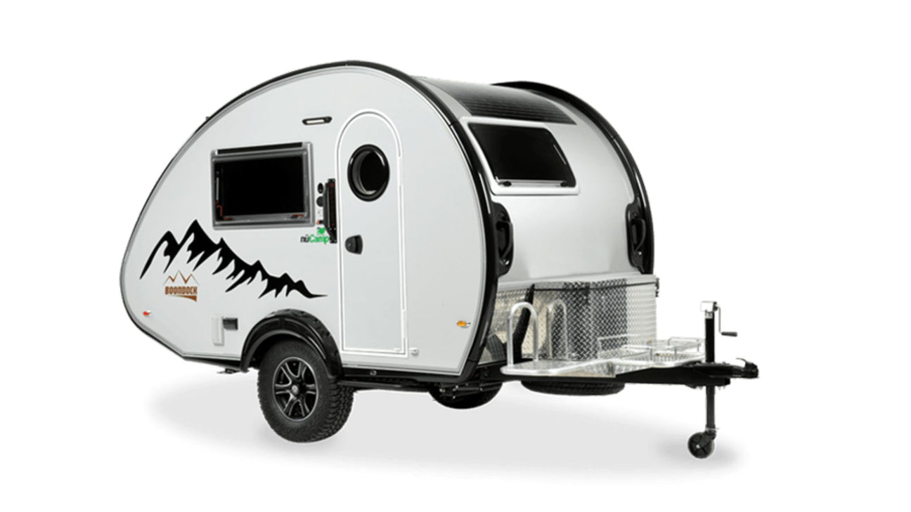 A compact white teardrop camper trailer with black accents, a side window, mountain graphics, and a front storage box, set against a plain white background.