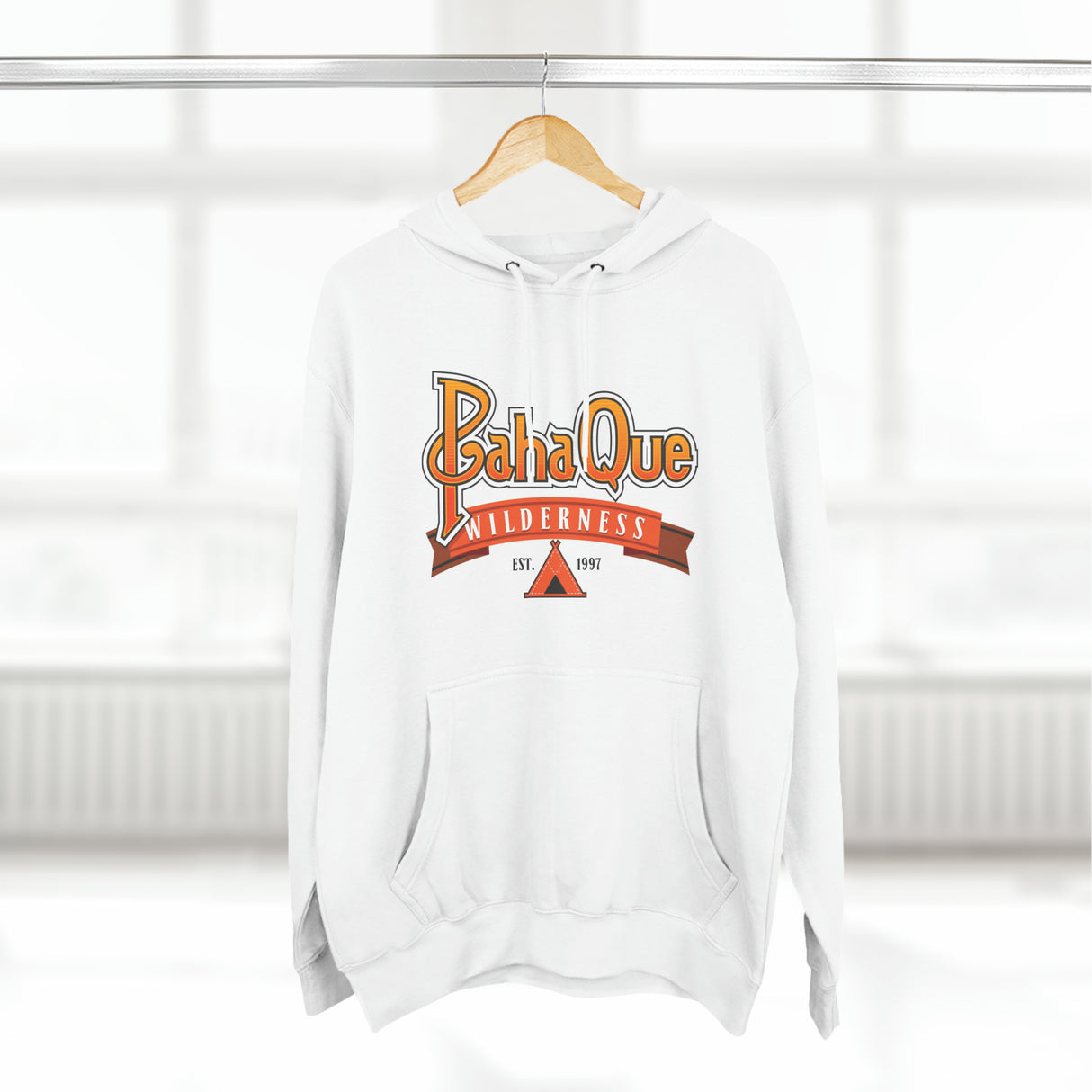The PahaQue Unisex Premium Pullover Hoodie in white by Printify hangs on a hanger, featuring a wilderness logo with a tent graphic and Est. 1997 in red and orange tones. Its cozy fleece lining is ideal for chilly days.