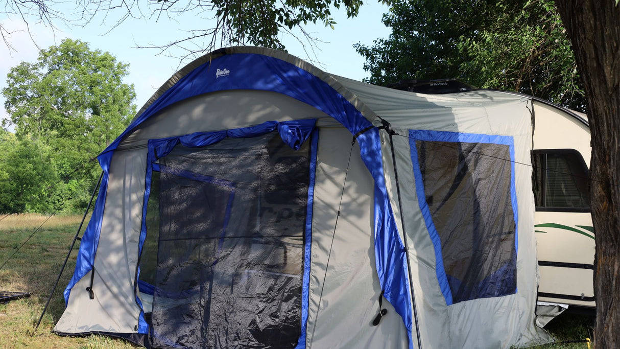 The Forest River R-Pod Trailer Side Tent by PahaQue Custom, shown attached to a white camper outdoors on lush grass, offers enhanced camping comfort and easy setup for nature getaways.