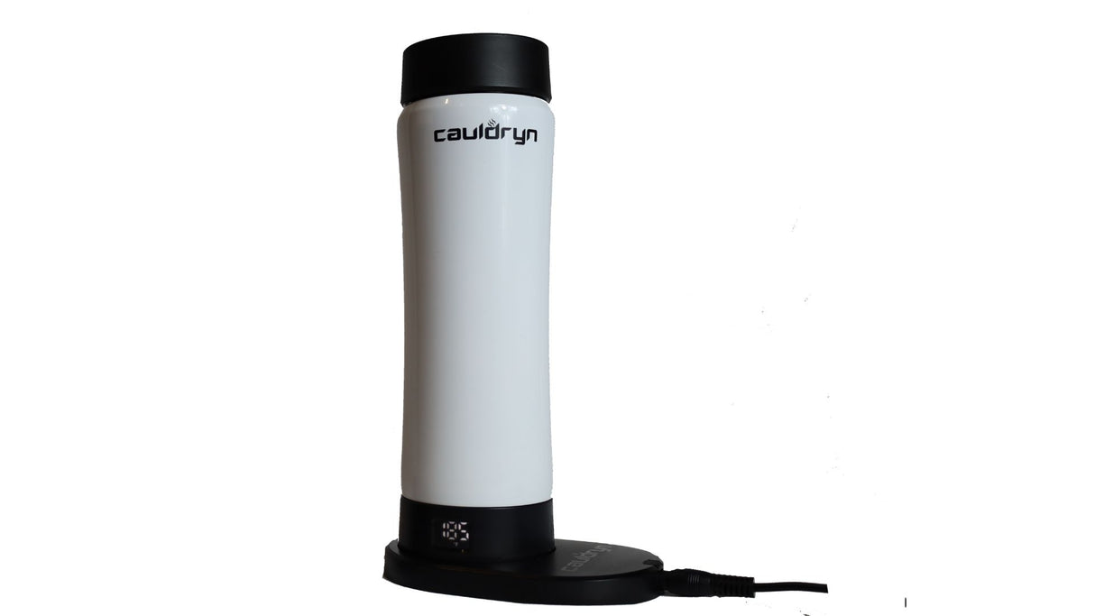 The Cauldryn Variable Temperature Beverage Warmer by PahaQue Wilderness is a tall, white, cylindrical electric appliance with black accents, upright on its circular charging dock connected by a cord.