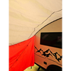 A close-up of a red and white tent by a camper trailer with a mountain design and window, shaded by the waterproof Paha Que Custom NuCamp TAB 360 Trailer Awning.