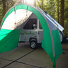 A small camper with a Paha Que Custom A-Frame Trailer Awning for Aliner, Chalet, Rockwood, and Jayco trailers (12ft–18ft) is set up in a sunlit forest among tall trees.