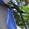Close-up of the Forest River R-Pod Trailer Side Tent by PahaQue, showing a blue rainfly, tent pole, and guy line with black connector—camping gear from Paha Que Custom—against a backdrop of blurred green leaves and trees.