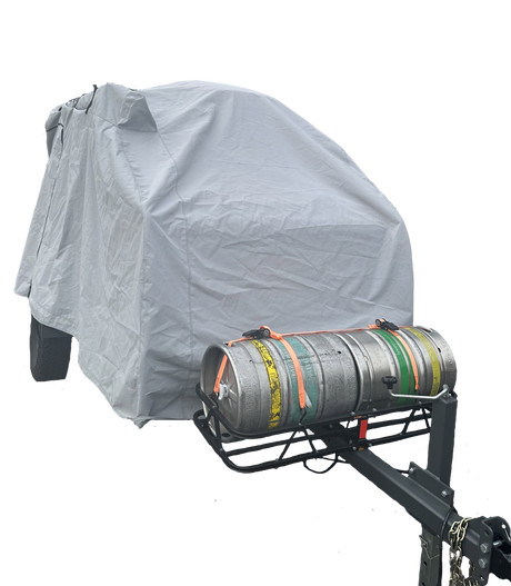 A vehicle is protected by a Paha Que Custom Campinawe Trailer Cover made of heavy-duty MagnaTuff fabric, with a front metal rack holding two strapped-down beer kegs—one silver, one striped.