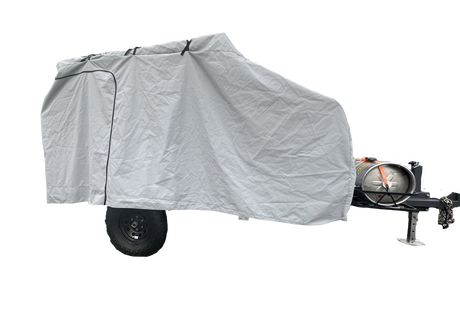 A Campinawe Trailer covered with the PahaQue Custom Heavy Duty MagnaTuff Fabric Trailer Cover features weather-proof, breathable material, a zippered side door, and reveals the metal tank, tow hitch, and black wheels at the front.