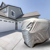 A large, light gray Paha Que Custom Meerkat Trailer Cover Heavy Duty MagnaTuff Fabric conceals a trailer in the driveway of a modern two-story house with green siding and three white garage doors under a clear sky.