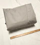 A folded Little Guy Mini Max FX Trailer Cover by PahaQue Wilderness in light gray lies on a white surface beside a wooden ruler for size reference. Made from durable MagnaTuff fabric.