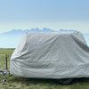 A small trailer sits on grass beneath a clear sky and hazy mountains, covered with the Hero Trailer Cover by Paha Que Custom, featuring heavy duty MagnaTuff fabric protection.
