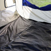 The photo shows the inside corner of the Forest River R-Pod Trailer Side Tent by Paha Que Custom, featuring a black floor, beige and white fabric walls, blue-topped window, and sunlight shining in—ideal for enhanced camping comfort.