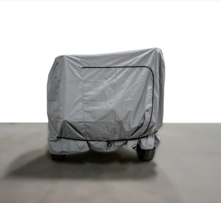 A large object on wheels is shielded indoors by a gray Paha Que Custom Off Grid Trailer Covers Premium Protection cover, featuring weather-resistant material, visible seams, and a drawstring base for optimal protection of most OffGrid trailers.