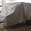 A trailer covered with a PahaQue Wilderness Sherpa Trailer Cover, made from durable MagnaTuff fabric, is parked indoors near a white wall, while two uncovered trailers can be seen in the background.