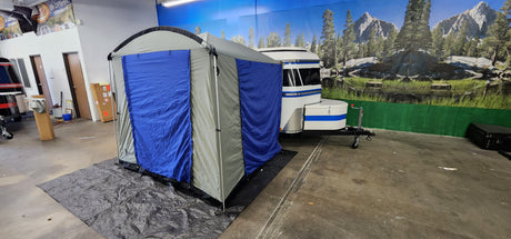 A Paha Que Custom Meerkat Trailer Side Tent for Enhanced Outdoor Adventures and Camping Comfort is set up indoors beside a Meerkat Trailer, with a scenic mural of mountains, trees, and a lake in the background.
