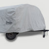 A trailer protected by a Teardrops Northwest Trailer Cover from PahaQue Wilderness, featuring a large fitted gray design with the PahaQue logo. The wheels and part of the hitch are partially visible beneath this custom-fit cover.