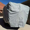 A large trailer is sheltered in a driveway by the Paha Que Custom Teton X Trailer Cover Premium Protection for TetonX Trailers, with a trash bin and red rocks visible in the background under a clear blue sky.