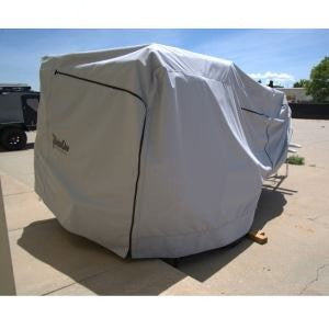 A Boreas Campers Trailer, protected by the Paha Que Custom Premium Trailer Cover, sits on a concrete driveway under clear skies, with trees and a fence in the background. The cover offers superior protection from the elements.