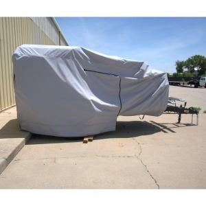 A large vehicle is shielded by the Boreas Campers Trailer Cover Premium Protection from Elements by Paha Que Custom and parked beside a yellow building on concrete under a clear blue sky.