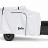 A Cedar Ridge camper is shielded by a white Cedar Ridge Vega XT AT Cover from Paha Que Custom for premium weather protection. Features include a single rugged tire, black storage box, and a metal jack stand at the front.
