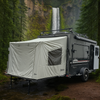A PahaQue Wilderness Custom Toy Hauler Patio Ramp Tent for Outdoor Adventures is set up in a lush green forest near a tall waterfall tumbling down a rocky cliff.