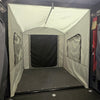 A PahaQue Wilderness Toy Hauler Patio Enclosure Ramp Tent, custom built to fit all toy hauler trailers, is attached to the back of a vehicle and features zippered windows and a door. The gray enclosure is viewed from inside the cargo area.
