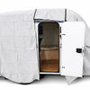 A small camper trailer fitted with the Paha Que Custom Meerkat Trailer Cover, made from heavy-duty MagnaTuff fabric for weather-resistant protection in gray, sits with its side door open to show a wooden floor and beige seating inside.