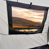 Enjoy the view from inside the Paha Que Custom NuCamp TAB 320 Trailer Side Tent for TAB and Boondock Trailers, with white and black fabric framing a grassy hill, pond, and vibrant sunset—highlighting this unique camping accessory.