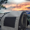 A Paha Que Custom NuCamp TAB 320 Trailer Side Tent for TAB and Boondock Trailers stands next to a trailer under a vivid orange sunset, surrounded by shrubs, trees, and distant mountains.