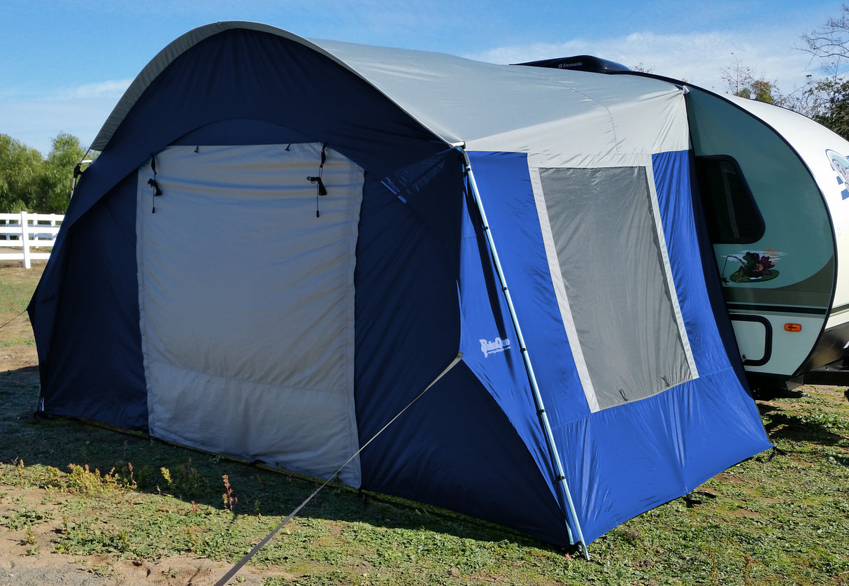 The Forest River R-Pod Trailer Side Tent by PahaQue Custom, attached to a white camper on grass with a white fence and trees behind, highlights easy setup and essential camping comfort for your outdoor adventures.