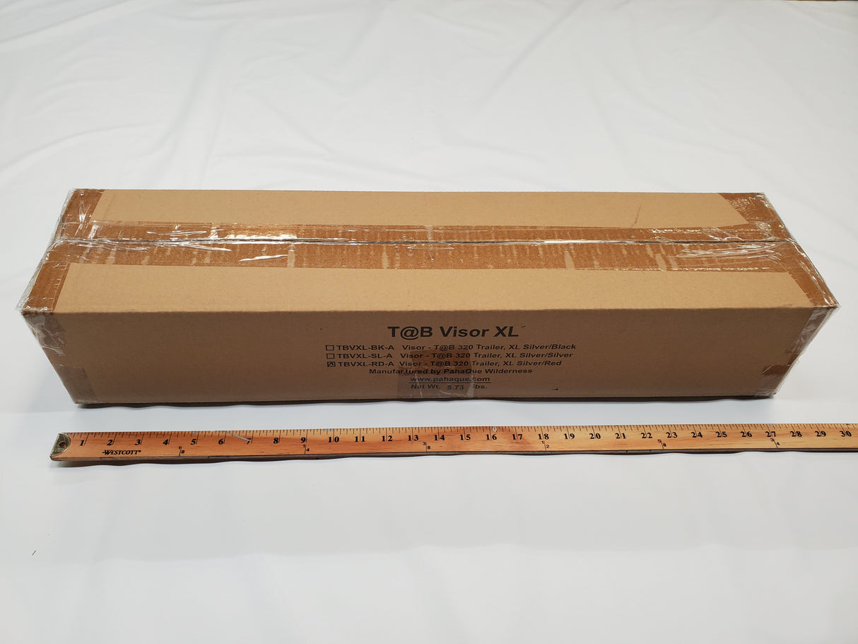 A rectangular Paha Que Custom NuCamp TAB 360 Trailer Visor Accessory box sits sealed on a white surface, with a ruler in front for scale—perfect for buyers seeking enhanced outdoor protection for their NuCamp TAB 360.