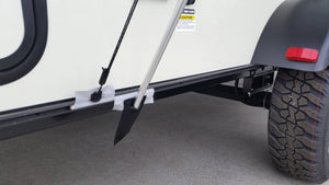 A close-up shows the Paha Que Custom R Pod Trailer Visor rod secured to the trailer frame with padding and tape, next to a rugged tire on concrete. Above this setup, a caution label is partially visible.