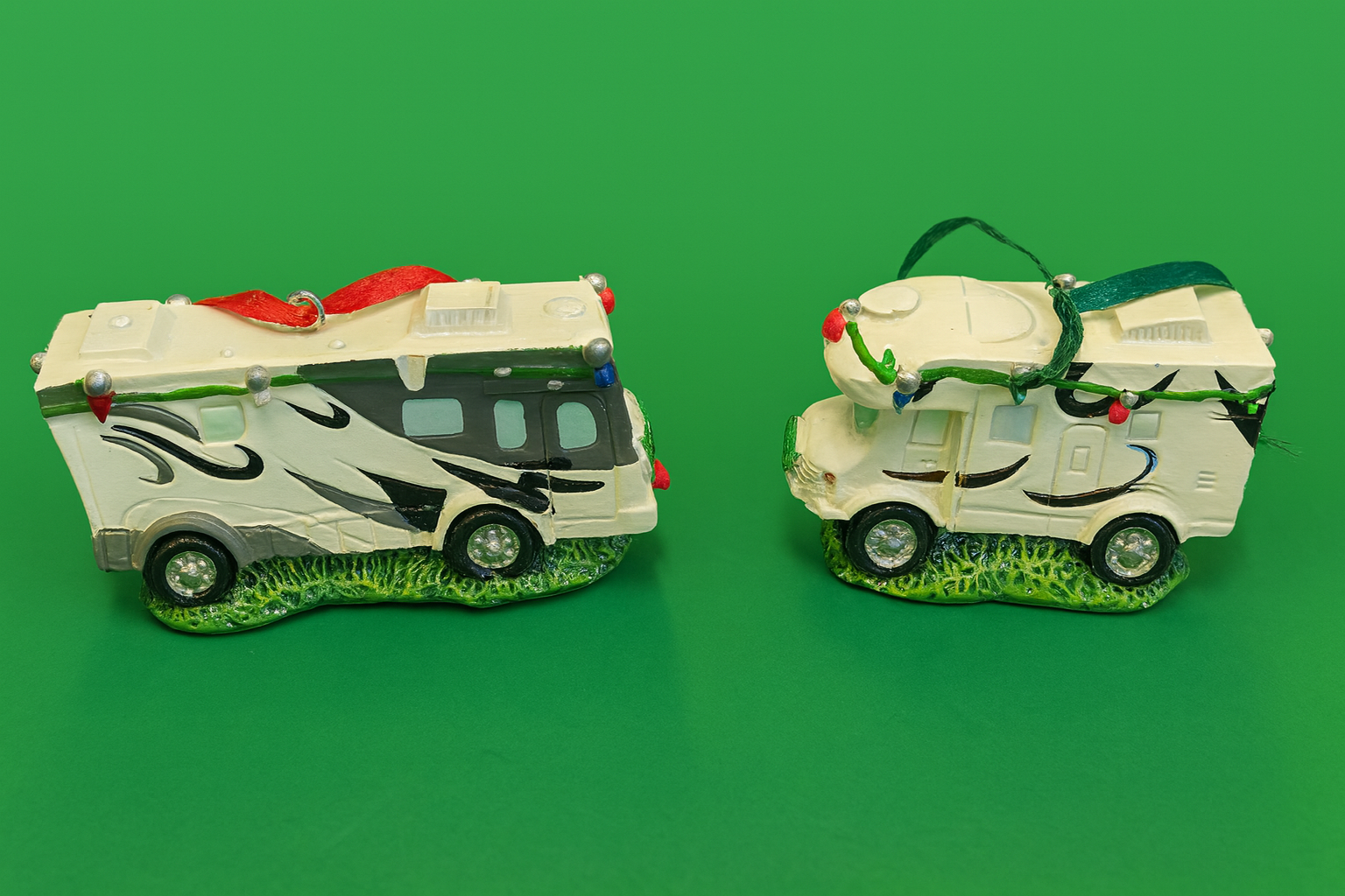 Part of the PahaQue Wilderness Christmas Collection, these two white Travel Trailer RV Ornaments feature black designs, green grass bases, and festive lights—ideal holiday décor for RV enthusiasts.