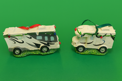 Part of the PahaQue Wilderness Christmas Collection, these two white Travel Trailer RV Ornaments feature black designs, green grass bases, and festive lights—ideal holiday décor for RV enthusiasts.