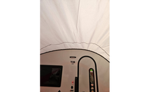 A view from inside a white Paha Que Custom NuCamp TAB 360 Trailer Awning, showing the curved roof, window, and door of a teardrop camper. The awnings waterproof fabric arches above the scene.