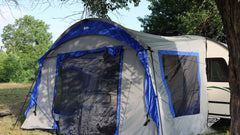 The Forest River R-Pod Trailer Side Tent by PahaQue Custom, shown attached to a white camper outdoors on lush grass, offers enhanced camping comfort and easy setup for nature getaways.