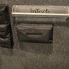 A gray wall with a metal inTech shelf and a PahaQue Wilderness Triple Gear Pouch Heavy Duty Gear Organizer for Trailers attached below, along with two smaller black pouches; part of a black and white object appears on the right.