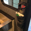 The PahaQue Wilderness Triple Gear Pouch Heavy Duty Gear Organizer for Trailers hangs by a metal sink in a modern RV kitchen, holding toiletries and grooming items. Sunlight from the window highlights this smart black storage solution.
