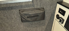 The PahaQue Wilderness PahaQue Gear Pouch, a black heavy-duty zippered pouch with Velcro patch, is attached to a gray felt wall beside a white panel with two black dials and display—ideal for organized trailer gear storage.
