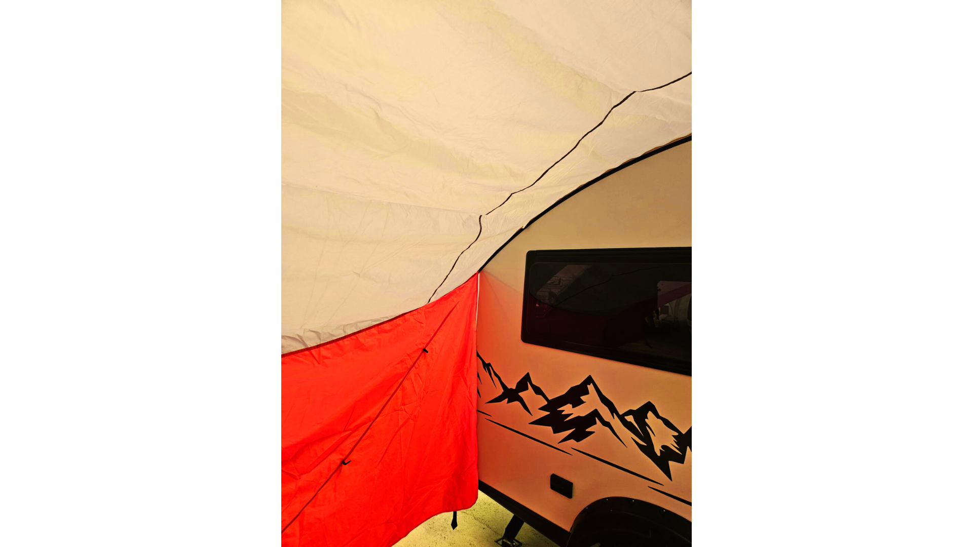 A close-up of a red and white tent by a camper trailer with a mountain design and window, shaded by the waterproof Paha Que Custom NuCamp TAB 360 Trailer Awning.
