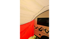 A close-up of a red and white tent by a camper trailer with a mountain design and window, shaded by the waterproof Paha Que Custom NuCamp TAB 360 Trailer Awning.