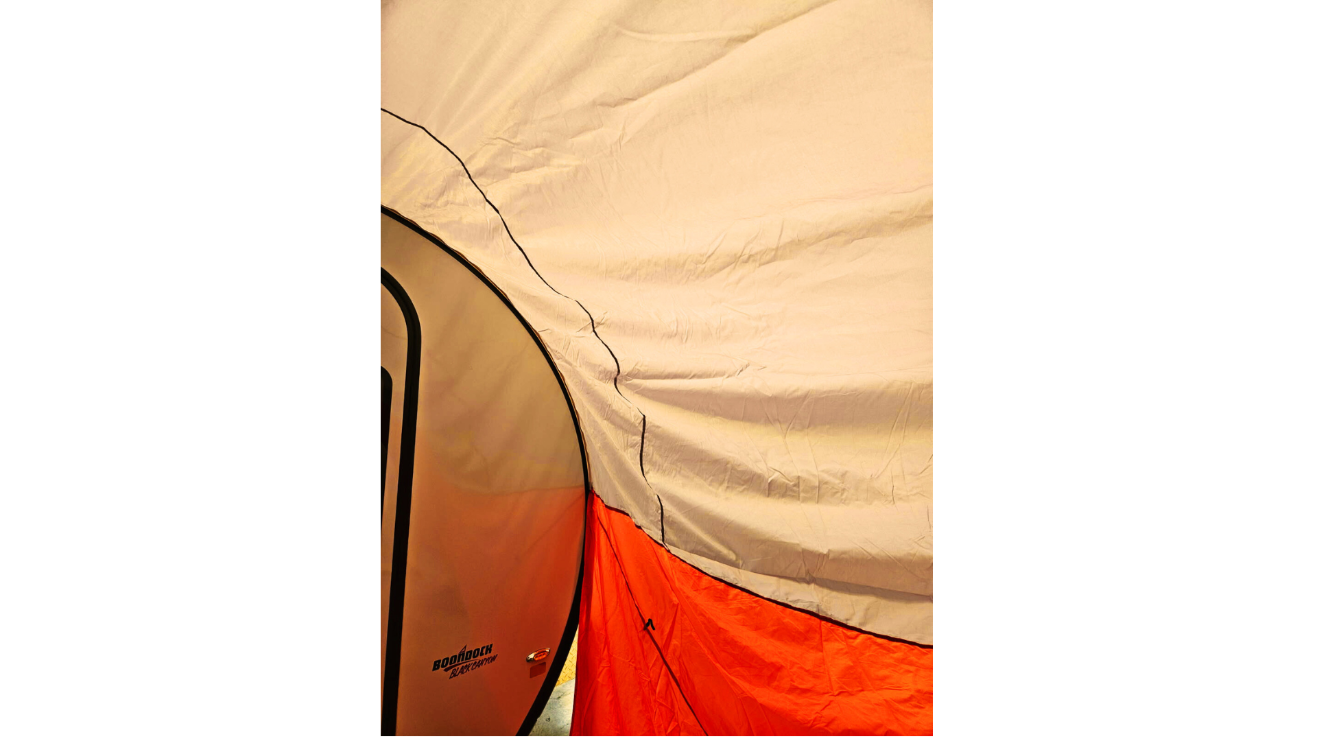 Close-up of a beige, orange, and white tent showing its fabric texture and seams, with part of a NuCamp TAB 360 Trailer Awning by Paha Que Custom and its teardrop camper visible on the left.