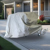 A trailer or small vehicle protected by the Ushi Chuck MAX Trailer Cover by PahaQue Custom appears to float above a driveway in front of a suburban house with a porch, landscaped yard, and garage.
