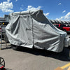 A vehicle sits outdoors covered by a Paha Que Custom Bean Trailer Covers Premium Durable Black Tailored Fit cover, protecting it under the sunny sky, with other vehicles and trailers visible in the background.