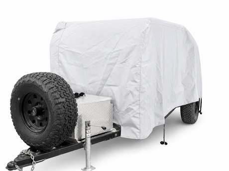A Colorado Teardrops Canyonland Pinnacle trailer outfitted with a white, custom-fit PahaQue Wilderness cover, a front-mounted spare tire, and a diamond-plate storage box by the hitch—perfect for your next adventure.