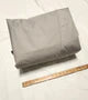 A folded Paha Que Custom Bushwhacker Plus Trailer Cover (Fits 15DS & 15FK, Made in USA) is placed on a white surface beside a wooden ruler to display the fabric's size.