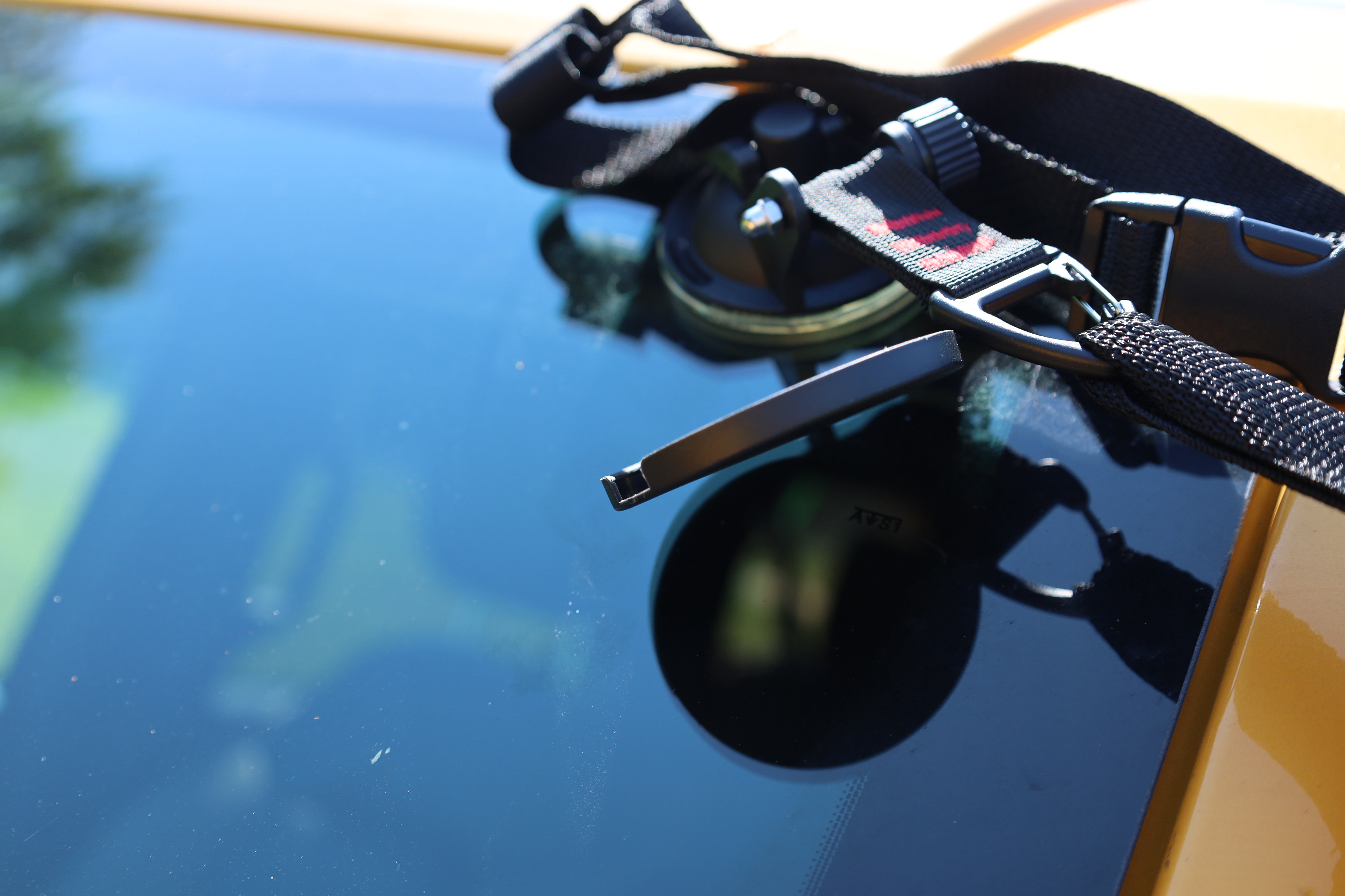 A black suction cup mount with adjustable strap secures the All Purpose Portable Vehicle Awning by PahaQue to a car’s windshield, making it easy to install for Cars, SUVs, Trucks, and Side by Sides. Brand: PahaQue Wilderness.