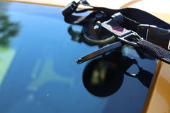 A black suction cup mount with adjustable strap secures the All Purpose Portable Vehicle Awning by PahaQue to a car’s windshield, making it easy to install for Cars, SUVs, Trucks, and Side by Sides. Brand: PahaQue Wilderness.