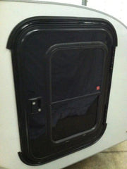 A close-up of a black rectangular camper door with a rounded frame and dark window, set in a light wall—ideal for use with the Paha Que Custom Mounting Kit for Trailer Side Tents 10x10 and 5x7.