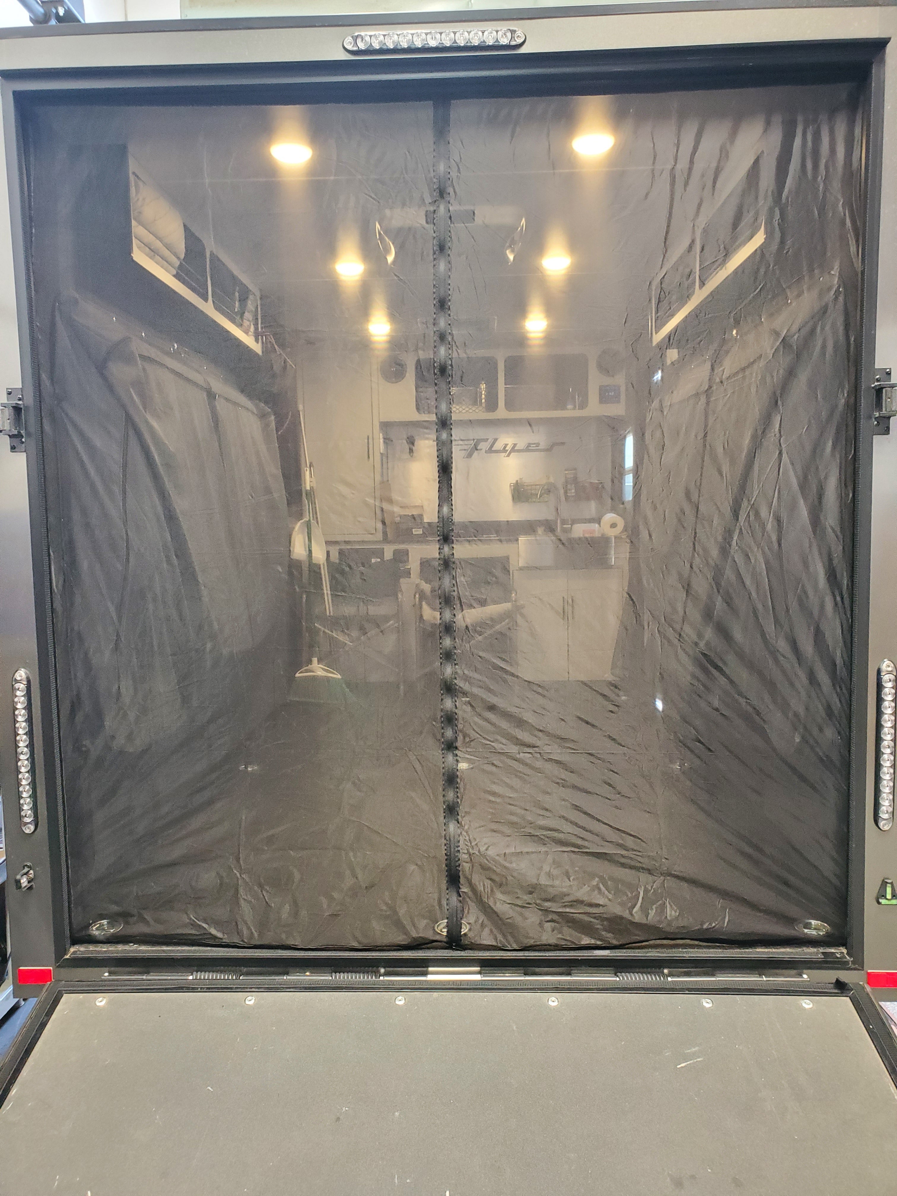 The Paha Que Custom Toy Hauler Mesh Door/Solid Room Divider covers your trailer or RV garage opening, offering a clear view inside with cabinets, lights, and counters while ensuring superior insect protection.