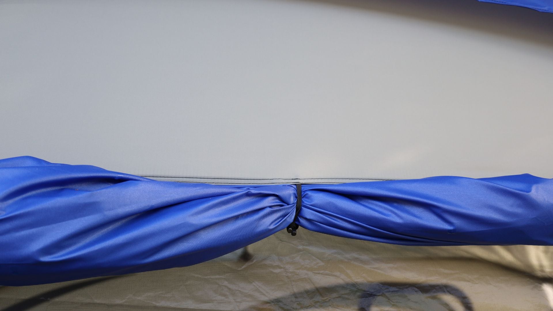 A close-up of the Forest River R-Pod Trailer Side Tent by PahaQue, showing a blue fabric secured with a black hook for easy setup—highlighting Paha Que Custom’s enhanced camping comfort against a light grey background.