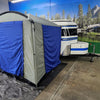 A Paha Que Custom Meerkat Trailer Side Tent for Enhanced Outdoor Adventures and Camping Comfort is set up indoors beside a Meerkat Trailer, with a scenic mural of mountains, trees, and a lake in the background.