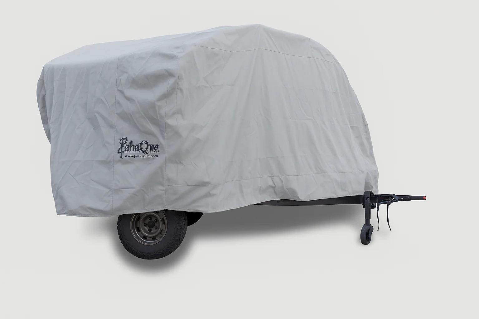 A trailer protected by a Teardrops Northwest Trailer Cover from PahaQue Wilderness, featuring a large fitted gray design with the PahaQue logo. The wheels and part of the hitch are partially visible beneath this custom-fit cover.